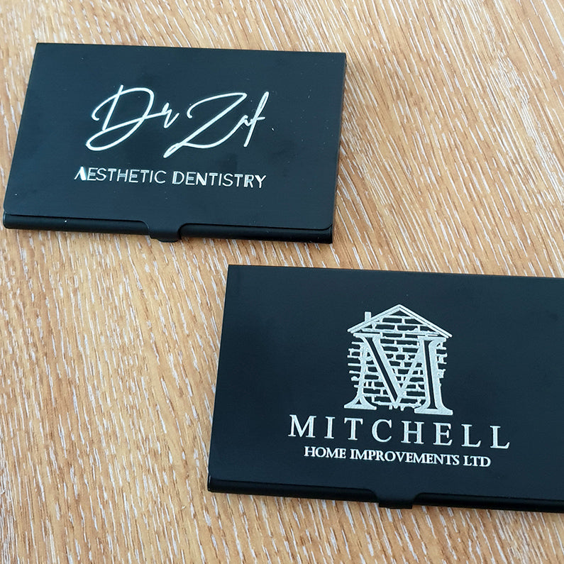 Two business cards on a wooden surface, one for 'Dr Zaif' Aesthetic Dentistry' and the other for 'Mitchell Home Improvements Ltd'.