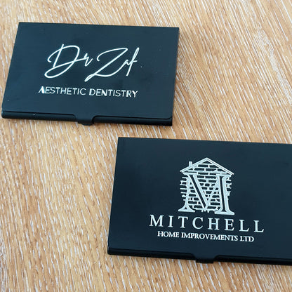 Two business cards on a wooden surface, one for 'Dr Zaif' Aesthetic Dentistry' and the other for 'Mitchell Home Improvements Ltd'.