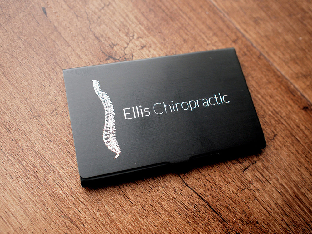 Black business card holder engraved with 'Ellis Chiropractic' and spinal illustration