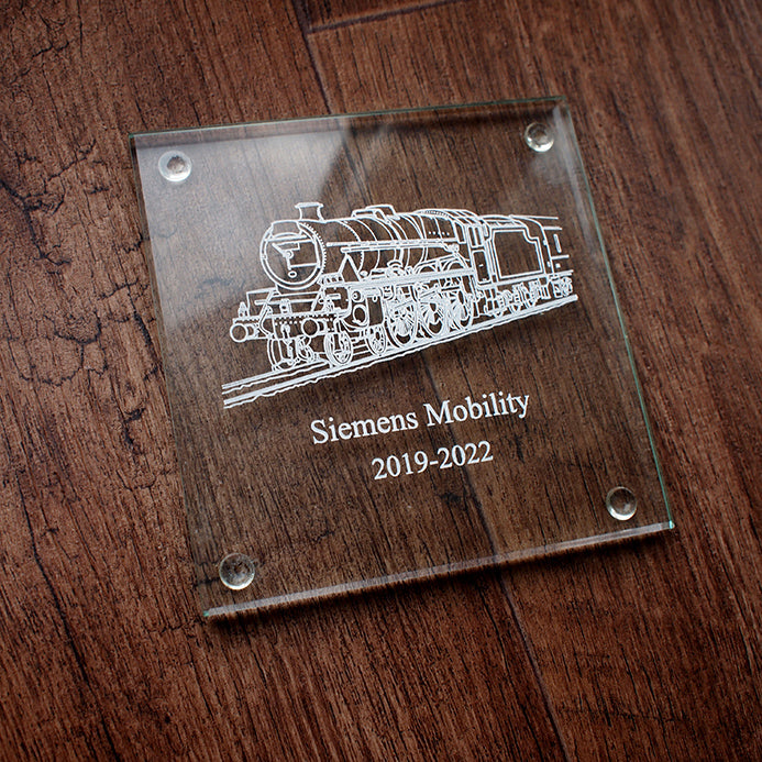 Glass plaque with steam train engraving and 'Siemens Mobility' text on a wooden surface