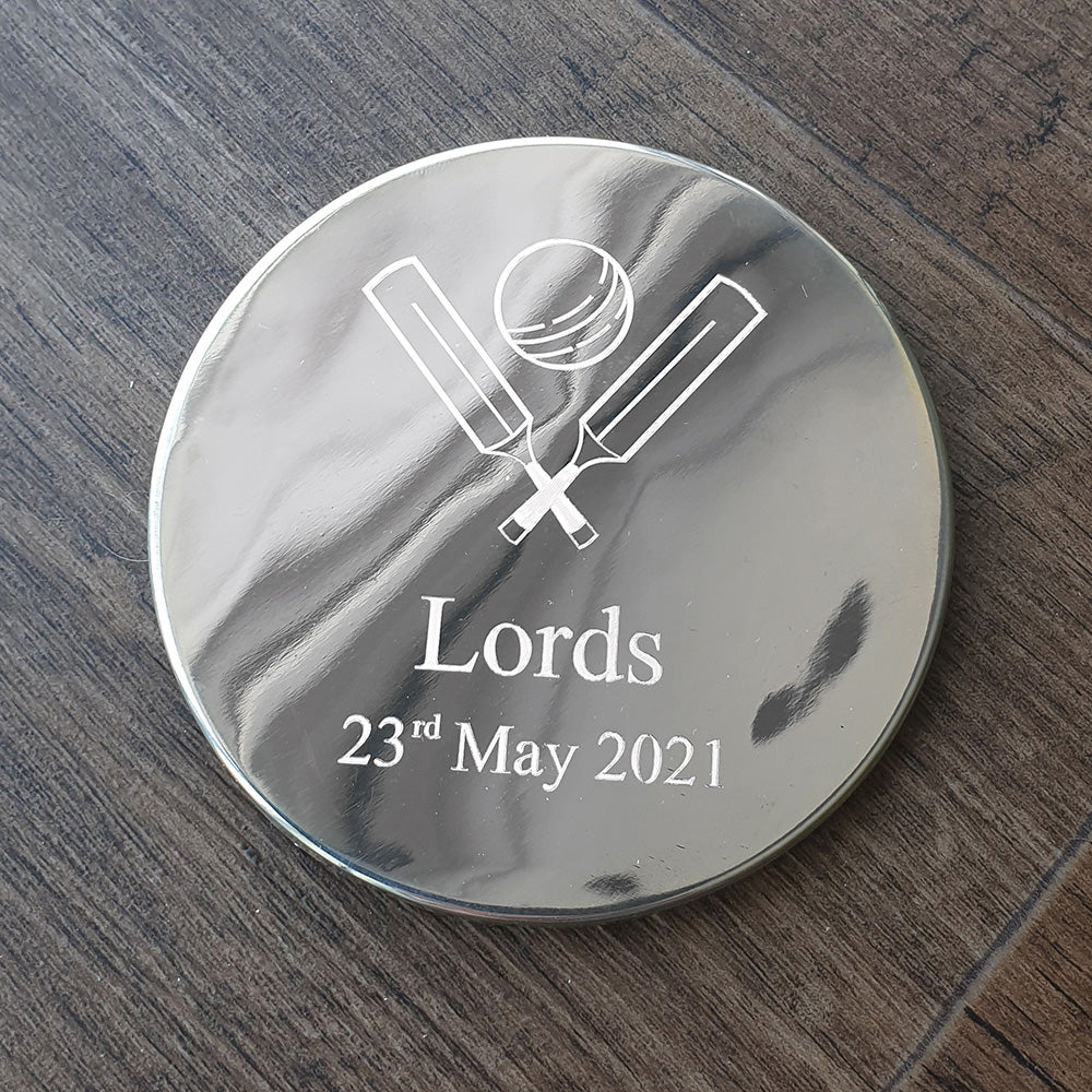 Round metallic object with cricket design and text on a wooden surface background