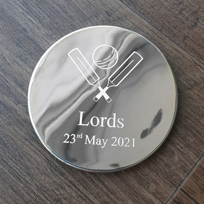 Round metallic object with cricket design and text on a wooden surface background