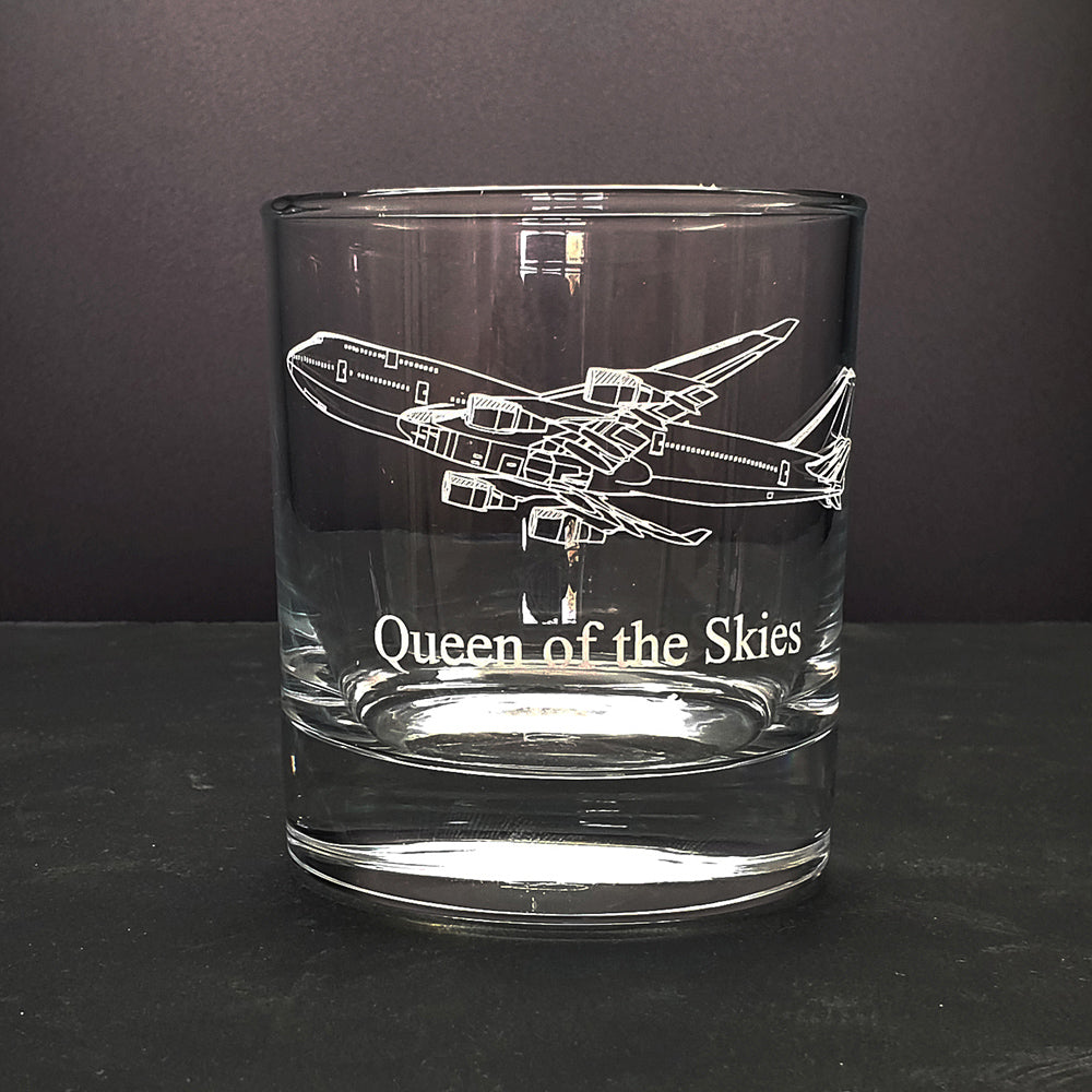 Clear glass tumbler with 747 artwork airplane engraving and 'Queen of the Skies' text on a dark background