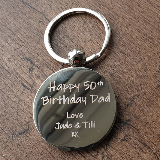 round chrome keychain with engraved  Birthday message to dad on a wooden surface