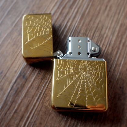 open brass petrol lighter with spider web design on a wooden surface background
