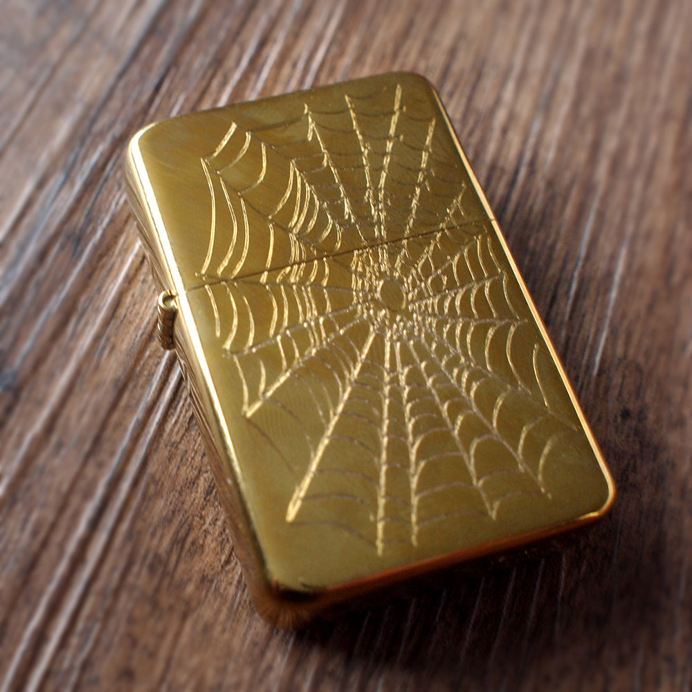 Gold lighter with spider web design on a wooden surface