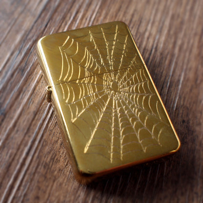 Gold lighter with spider web design on a wooden surface