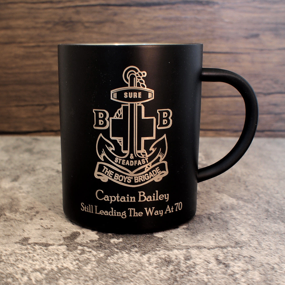 Black mug with engraved design and text on a stone surface with wooden background