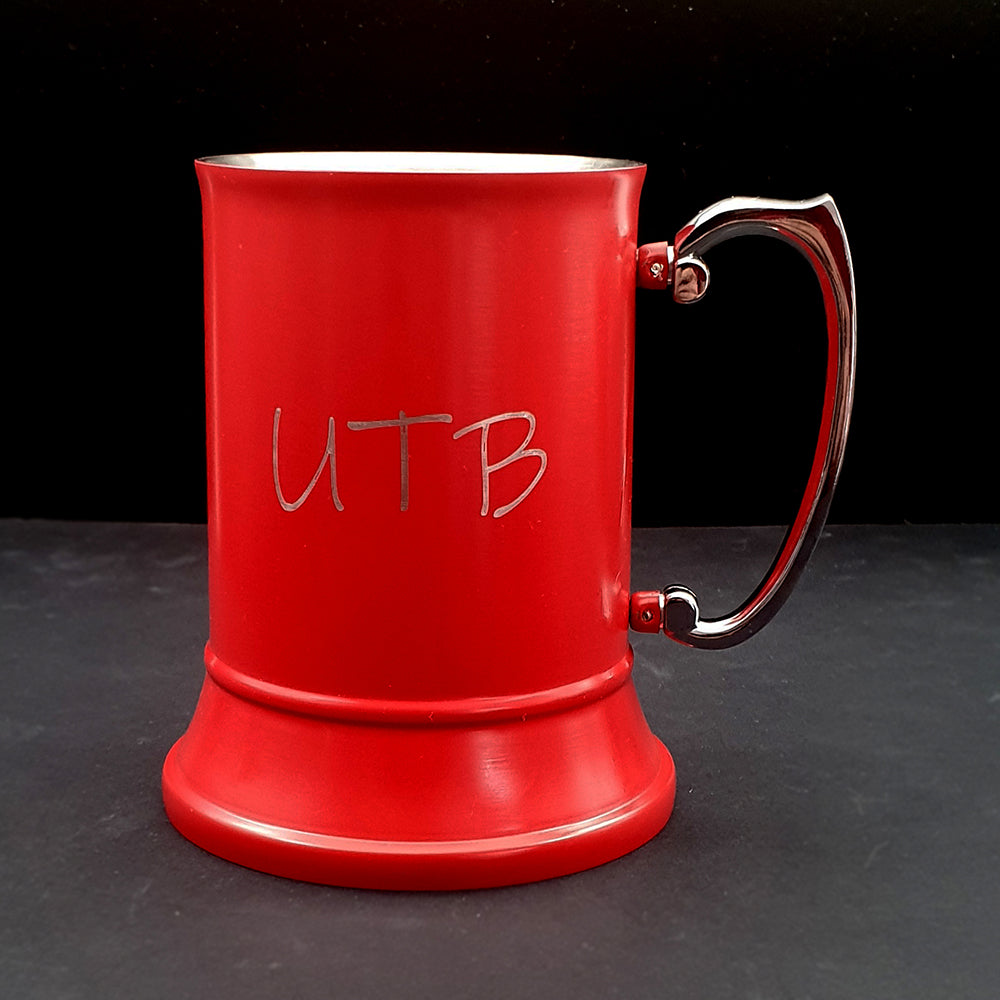Red steel mug with 'UTB' engraving on a dark surface