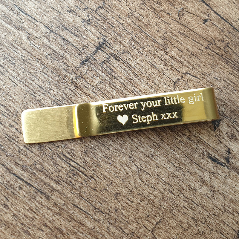 Gold tie clip with engraved message on a wooden surface background
