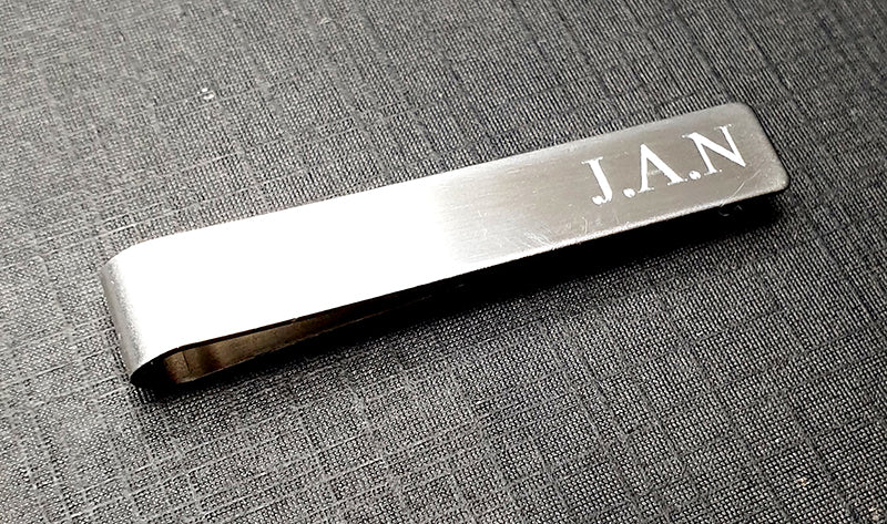 Silver tie clip with JAN engraving on a textured grey surface background