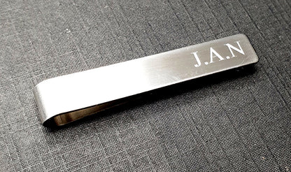 Silver tie clip with JAN engraving on a textured grey surface background