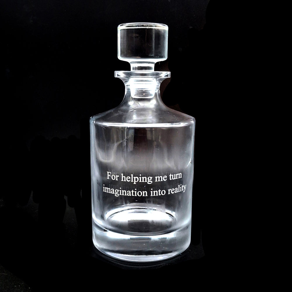 Clear glass round decanter with engraved text on a black background