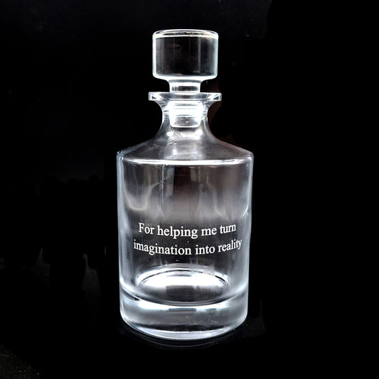 Clear glass round decanter with engraved text on a black background