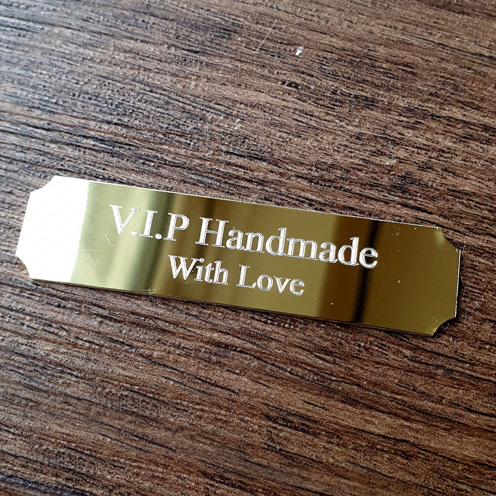 Gold tag with 'V.I.P Handmade With Love' text on a wooden surface