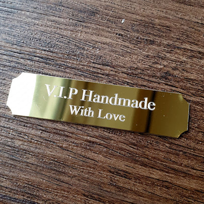 Gold tag with 'V.I.P Handmade With Love' text on a wooden surface