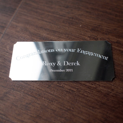 Silver cut corner plaque engraved with 'Congratulations on your Engagement' card on a wooden surface background